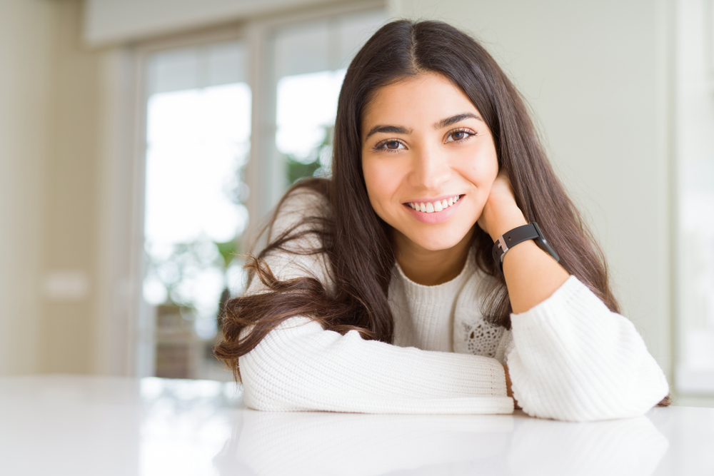 Woman smiling warmly indoors, showcasing a bright, even smile enhanced by custom porcelain veneers – Austin TX Veneers