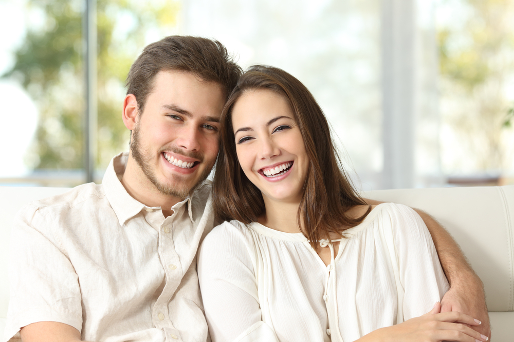 Happy couple relaxes at home with bright, healthy smiles made possible through consistent preventative dental care and regular checkups – Preventative