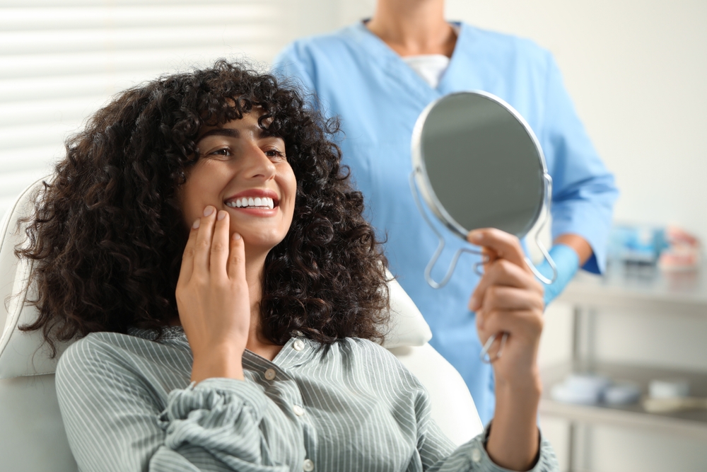 Smiling patient holding a mirror after dental crown treatment, showing confidence and satisfaction with restored teeth – Austin TX Dental Crowns
