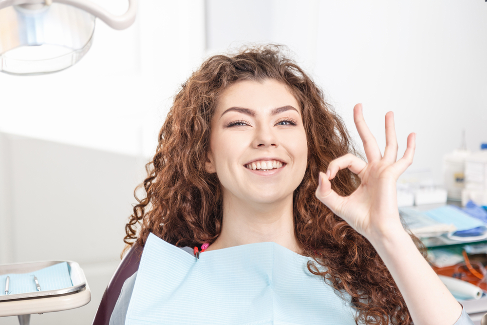 Smiling patient giving an OK sign after a teeth cleaning, reflecting fresh results and excellent oral hygiene care – Teeth Cleaning in Austin