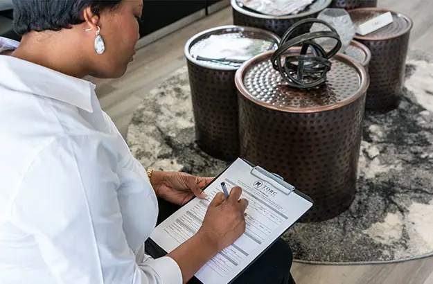 Patient completing registration paperwork in waiting area – TORC Dental Woman filling out new patient forms on a clipboard while seated in the TORC Dental waiting area with modern decor – TORC Dental