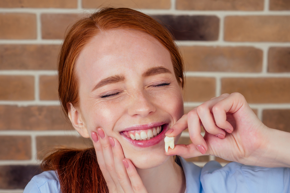 Smiling patient holding an extracted wisdom tooth, representing relief, recovery, and successful wisdom teeth removal treatment – Wisdom Teeth Removal in Austin